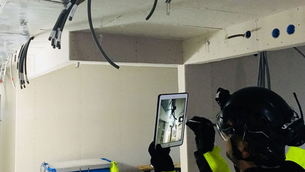 Person fotar kablar i ett tak med en surfplatta.