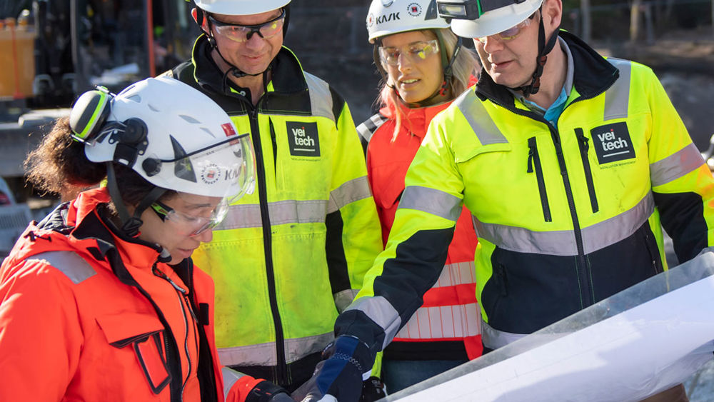 Flera personer i varselkläder samtalar kring en ritning.