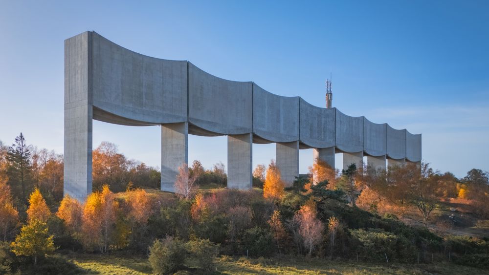 Arkitektbild där Våga vattentorn höjer sig som en våg längs med horisonten mot en fond av höstträd