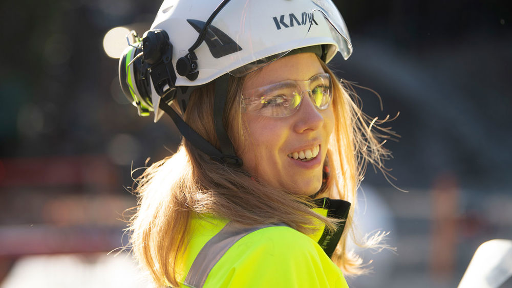 Leende tjej i varselkläder och skyddshjälm.